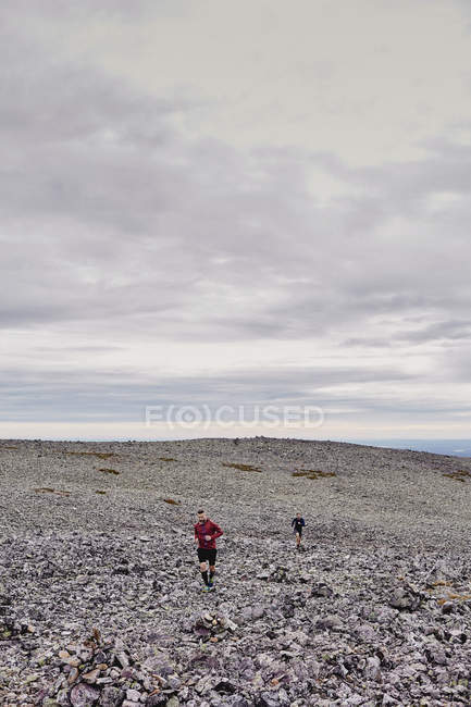 Двое мужчин вместе бегут по скалам, Остленд, Финляндия — стоковое фото