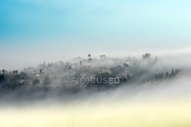 Vista da aldeia nebulosa em montanhas contra o céu azul — Fotografia de Stock