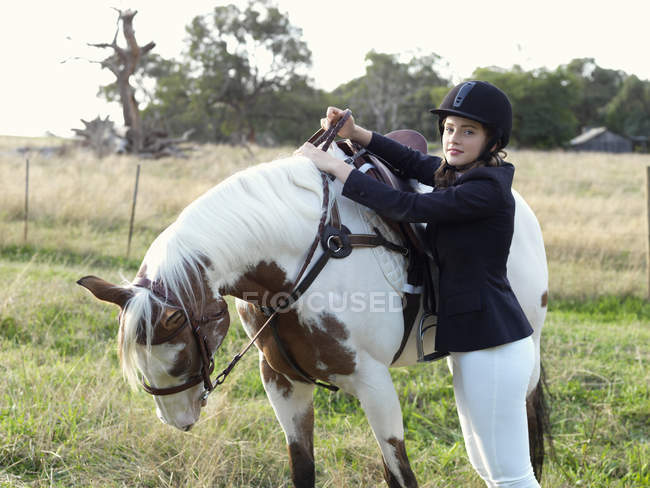 Portrait of teenage girl preparing to mount horse — Stock Photo