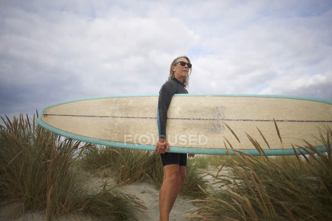 Портрет старшої жінки на піску, що тримає дошку для серфінгу — стокове фото