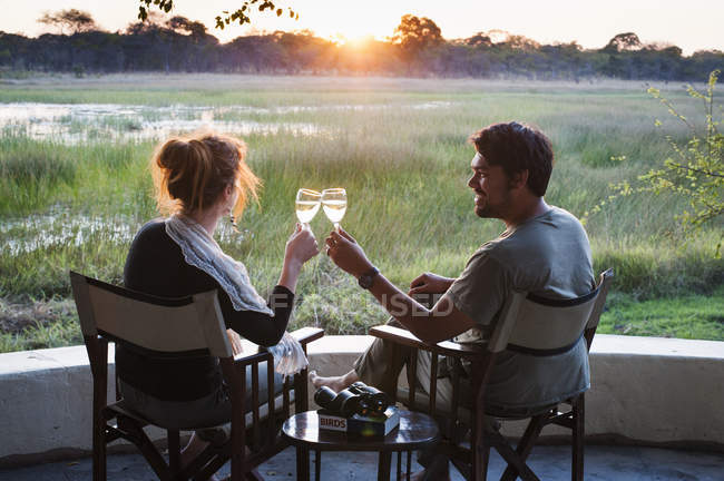 Casal com vinho branco no safari lodge durante o pôr do sol — Fotografia de Stock