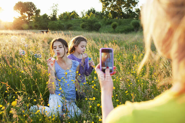 Mother taking photograph of girls blowing bubbles — Stock Photo