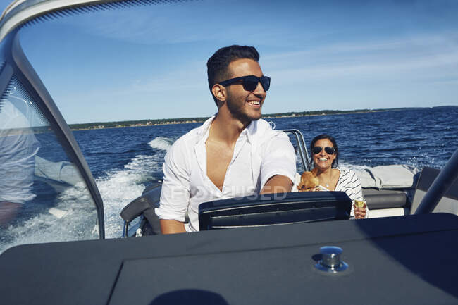 Hombre joven dirigiendo barco con mujer en el fondo, Gavle, Suecia - foto de stock
