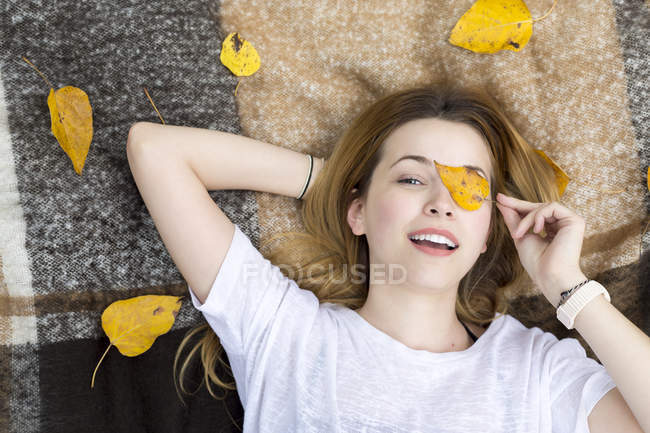 Молодая женщина лежит на одеяле, закрывая глаза листьями — стоковое фото