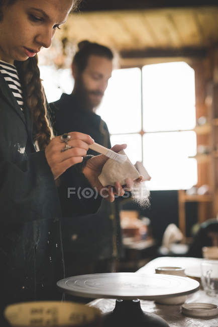 Side view of young woman in workshop brushing clay pot — Stock Photo