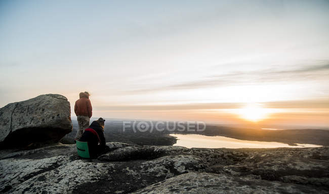 Dos jóvenes excursionistas mirando al atardecer sobre un lago distante - foto de stock