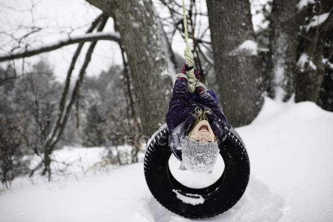 Ragazza a testa in giù su pneumatico swing in neve — Foto stock