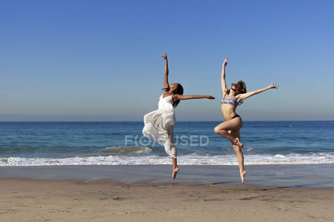 Дві молоді жінки-танцюристи стрибають середнє повітря на пляжі — стокове фото