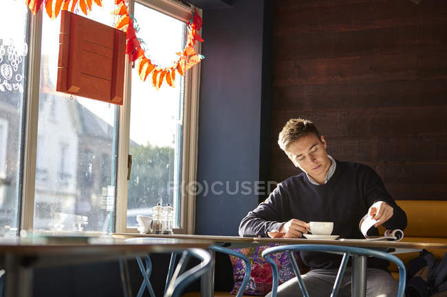 Young man alone in cafe drinking coffee and reading magazine — Stock Photo