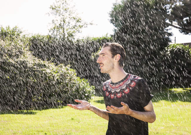 Junger Mann steht unter Gartensprenger — Stockfoto