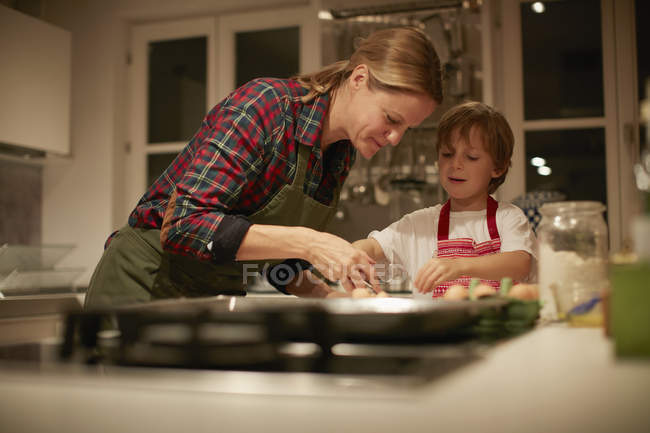 Зрелая женщина помогает сыну с выпечкой на кухне — стоковое фото