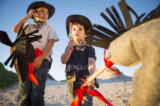 Dois irmãos vestidos de cowboys com arma de brinquedo e cavalos de passatempo — Fotografia de Stock