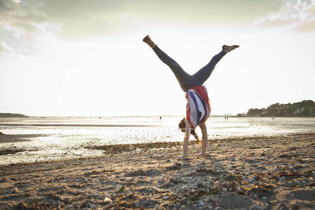 Молодая женщина делает стойку на руках на пляже Борнмут, Дорсет, Великобритания — стоковое фото