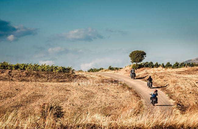 Vista trasera de cuatro amigos montando motocicletas en carretera rural, Cagliari, Cerdeña, Italia - foto de stock