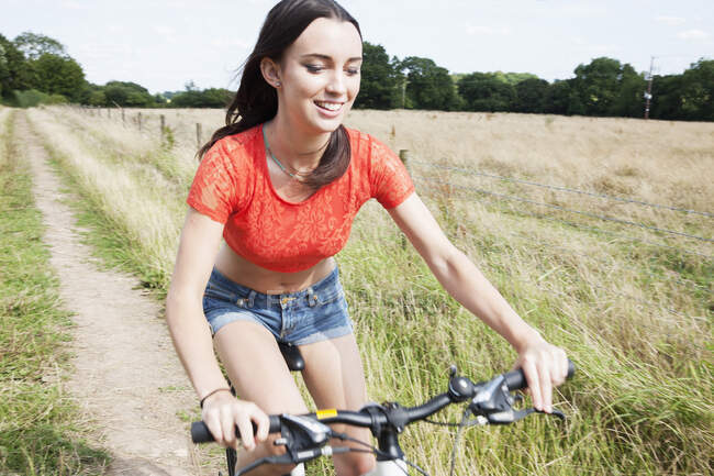 Giovane donna in bicicletta su pista sterrata in campo — Foto stock