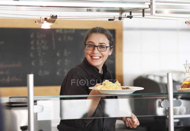 Woman working in restaurant kitchen, serving meal — Stock Photo