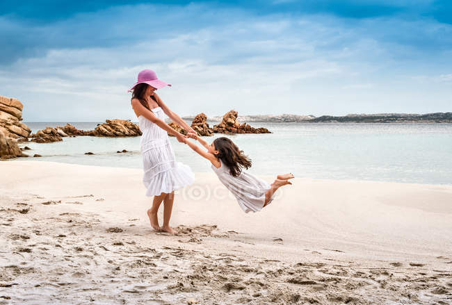 Giovane donna dondolante figlia sulla spiaggia, La Maddalena, Sardegna, Italia — Foto stock