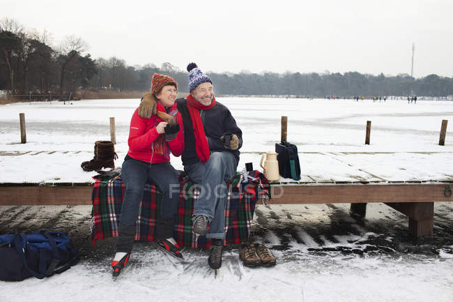 Couple sitting on pier having hot drink — Stock Photo