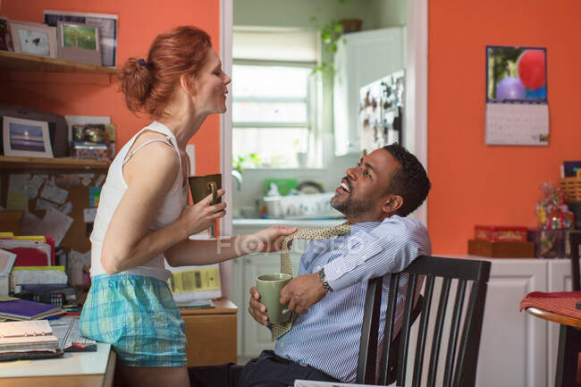Mature couple in kitchen, woman pulling man's tie — Stock Photo