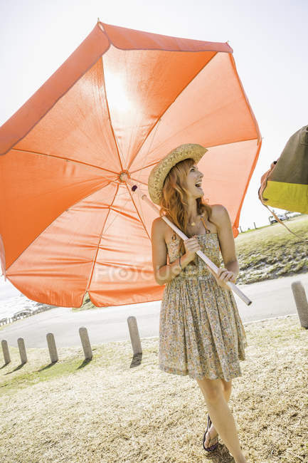Mid adult woman carrying red beach umbrella at beach, Cape Town, South Africa — Stock Photo