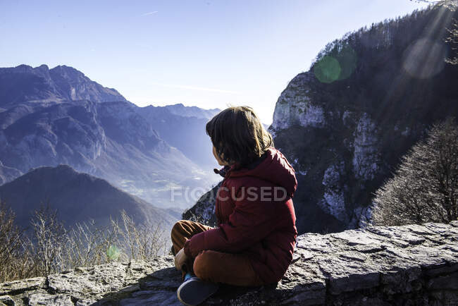 Ragazzo seduto sul muro che guarda il paesaggio montano, Italia — Foto stock