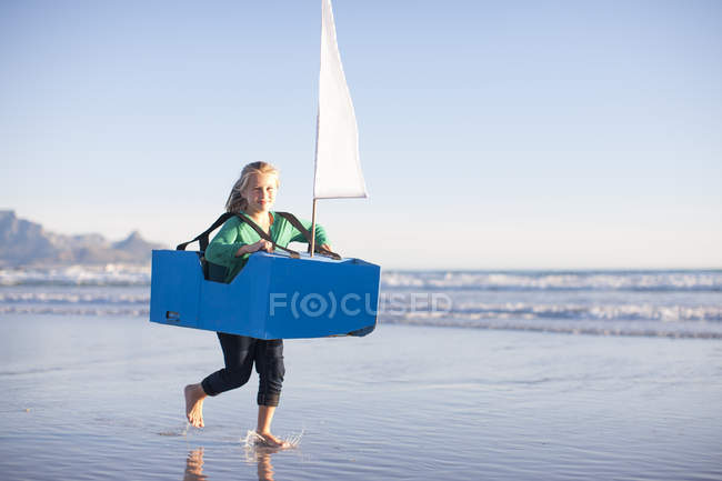 Mädchen läuft mit Spielzeugboot am Strand entlang — Stockfoto