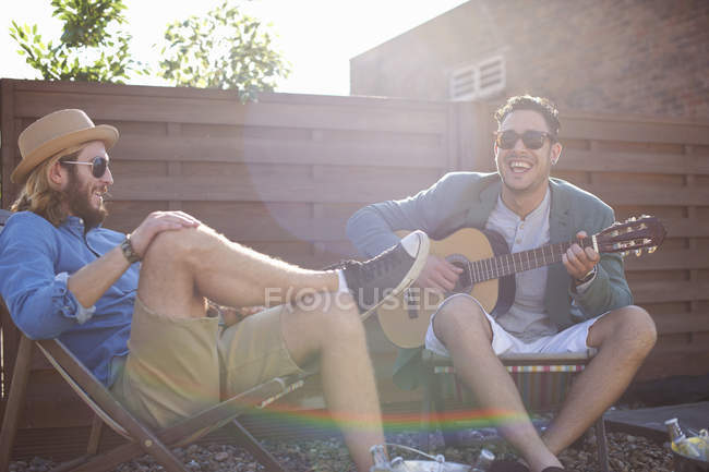 Dos amigos varones tocando la guitarra en la fiesta en la azotea - foto de stock