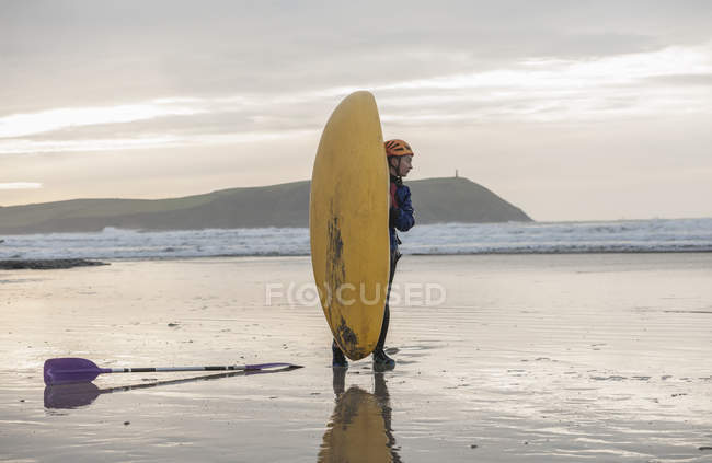 Mujer joven en la playa con kayak de mar, Polzeath, Cornwall, Inglaterra - foto de stock