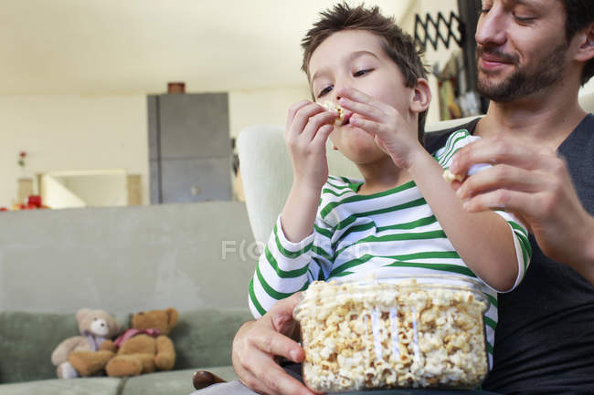 Padre e hijo comparten palomitas de maíz en la sala de estar - foto de stock