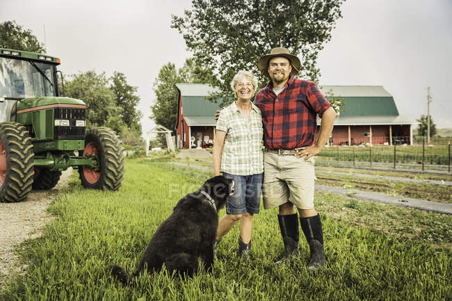 Мать и сын с собакой на ферме смотрят в камеру улыбаясь — стоковое фото