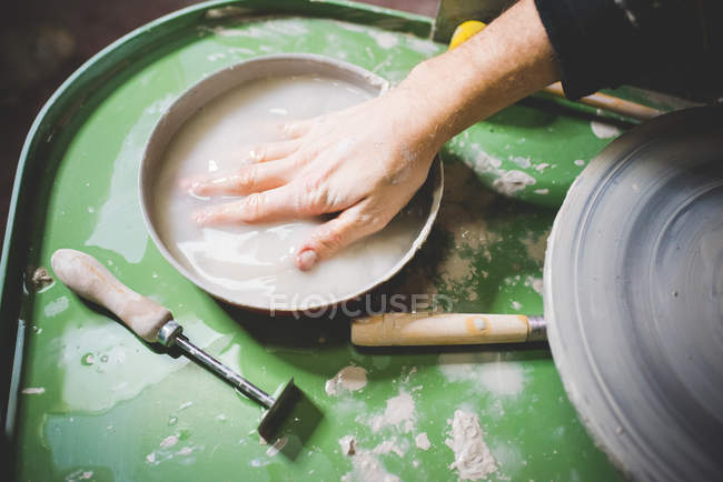 Main masculine adulte moyenne immergée dans un bol d'eau sur une roue de poterie — Photo de stock