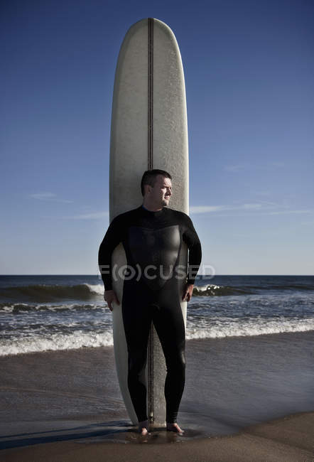 Portrait of mature man standing with tall surfboard on beach — Stock Photo