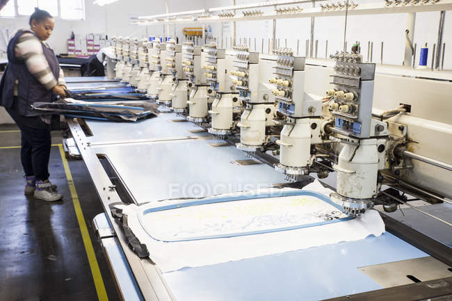 Trabalhadora da fábrica feminina preparando pano para costura de velocidade programada máquina de bordado na fábrica de roupas — Fotografia de Stock