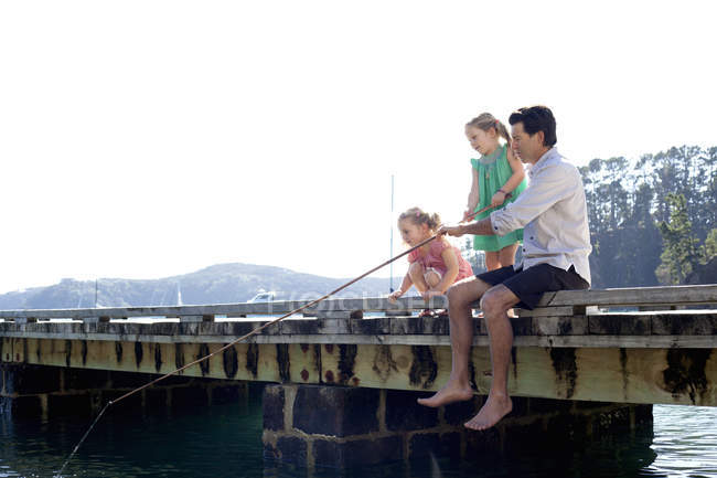 Зрелый мужчина и дочери рыбачат на морском пирсе, Новая Зеландия — стоковое фото