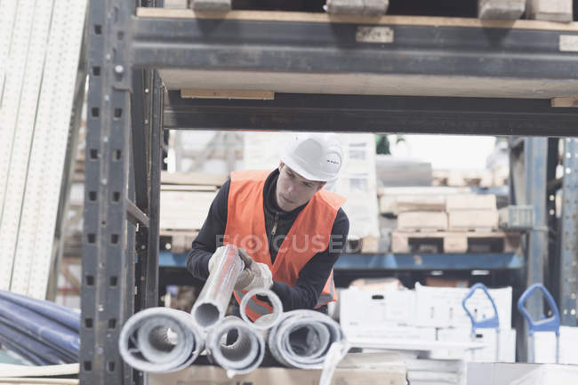 Young male warehouse worker selecting industrial pipe from shelf — Stock Photo