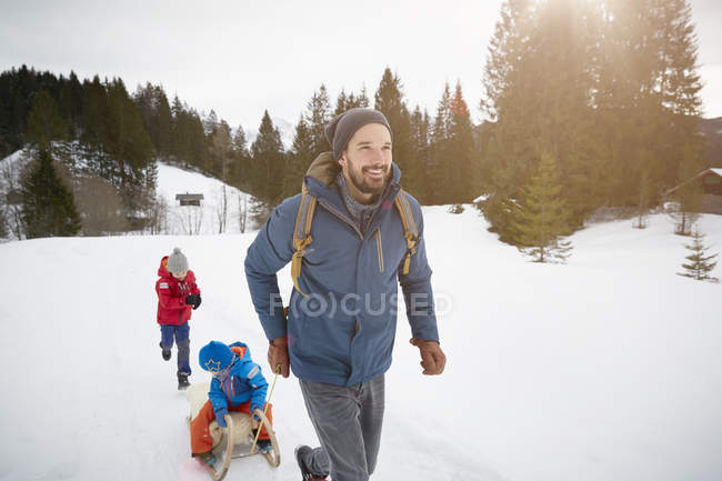 Young man pulling sons on toboggan in snow covered landscape, Elmau, Bavaria, Germany — Stock Photo