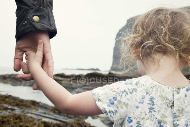 Image recadrée d'une fillette tenant la main de son père alors qu'elle se promenait sur la plage, Crackington Haven, Cornouailles — Photo de stock