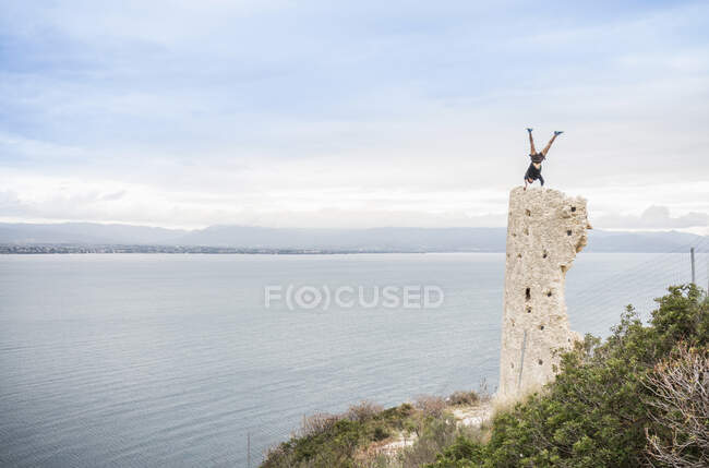 Bergsteiger beim Handstand auf einem zerstörten Turm an der Küste, Cagliari, Italien — Stockfoto