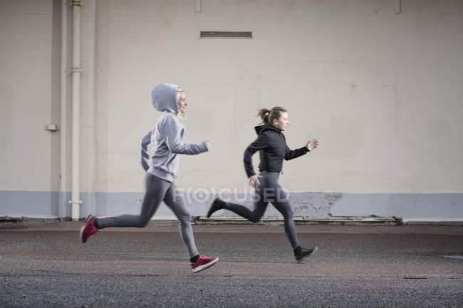 Two female runner friends running on urban road — Stock Photo
