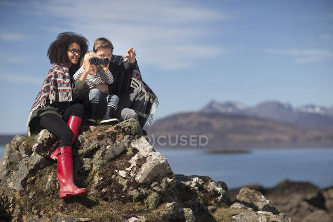 Familia sentada en las rocas, niño usando prismáticos - foto de stock