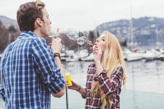 Young couple on waterfront blowing bubbles at each other, Lake Como, Italy — Stock Photo