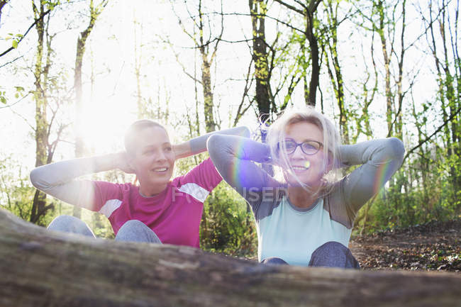 Mujeres en manos del bosque detrás de la cabeza haciendo sentarse contra el árbol caído - foto de stock