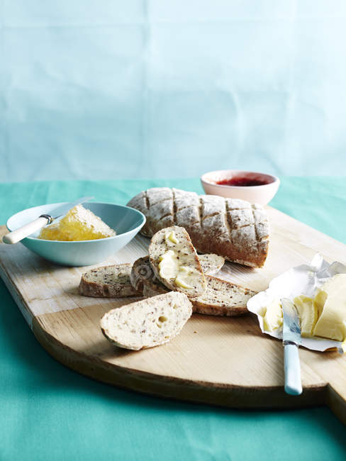 Tabla de cortar con pan fresco sin amasar con miel, mantequilla y mermelada - foto de stock
