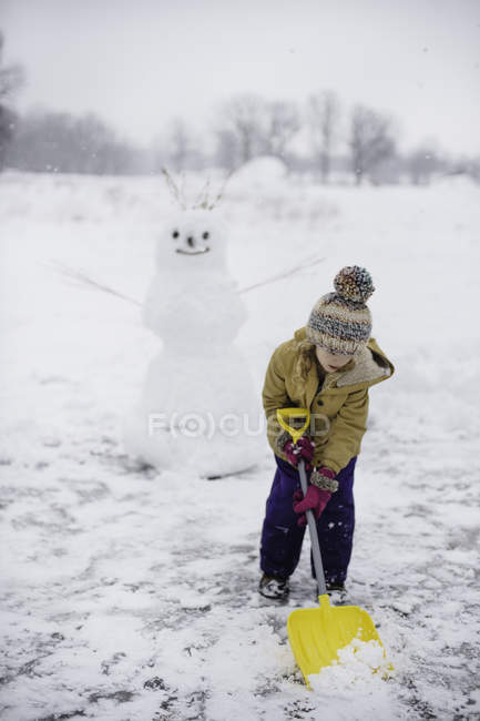 Fille pelletant de la neige devant un bonhomme de neige, Lakefield, Ontario, Canada — Photo de stock