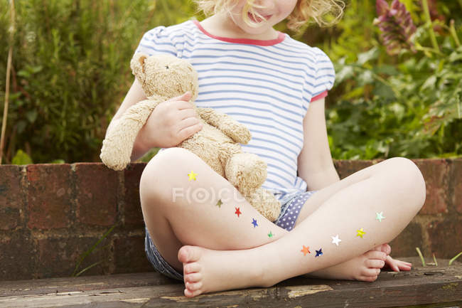 Girl on garden seat with star stickers on legs — Stock Photo