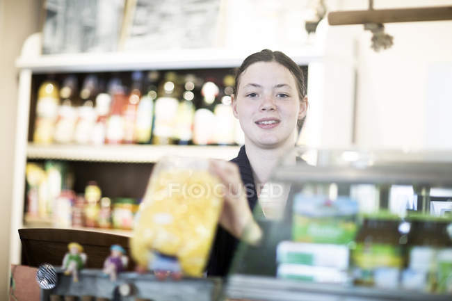 Portrait of young female shop assistant at corner shop counter — Stock Photo