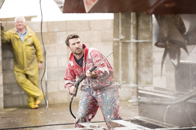 Male ship painter cleaning ship hull with pressure washer in ship painters yard — Stock Photo