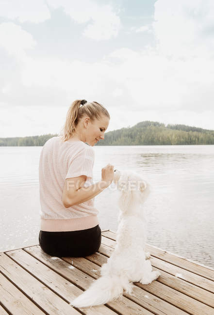 Женщина гладит котонную собаку на озерном пирсе, Оривеси, Финляндия — стоковое фото