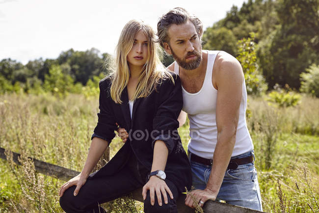 Portrait of couple sitting on rural fence looking sideways — Stock Photo