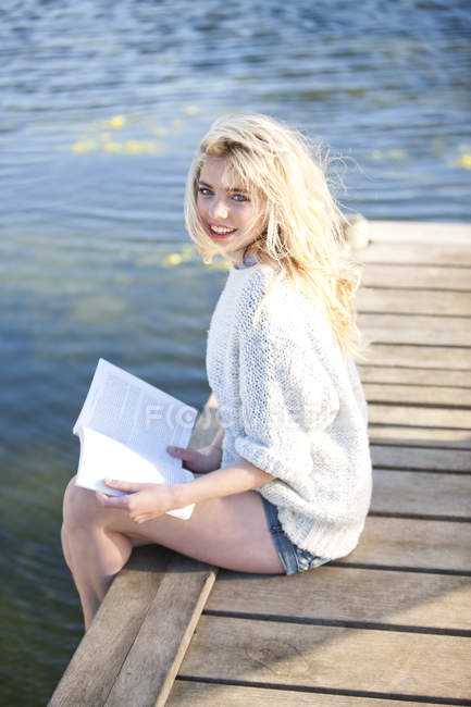 Junge Frau sitzt auf Seebrücke und hält Buch — Stockfoto